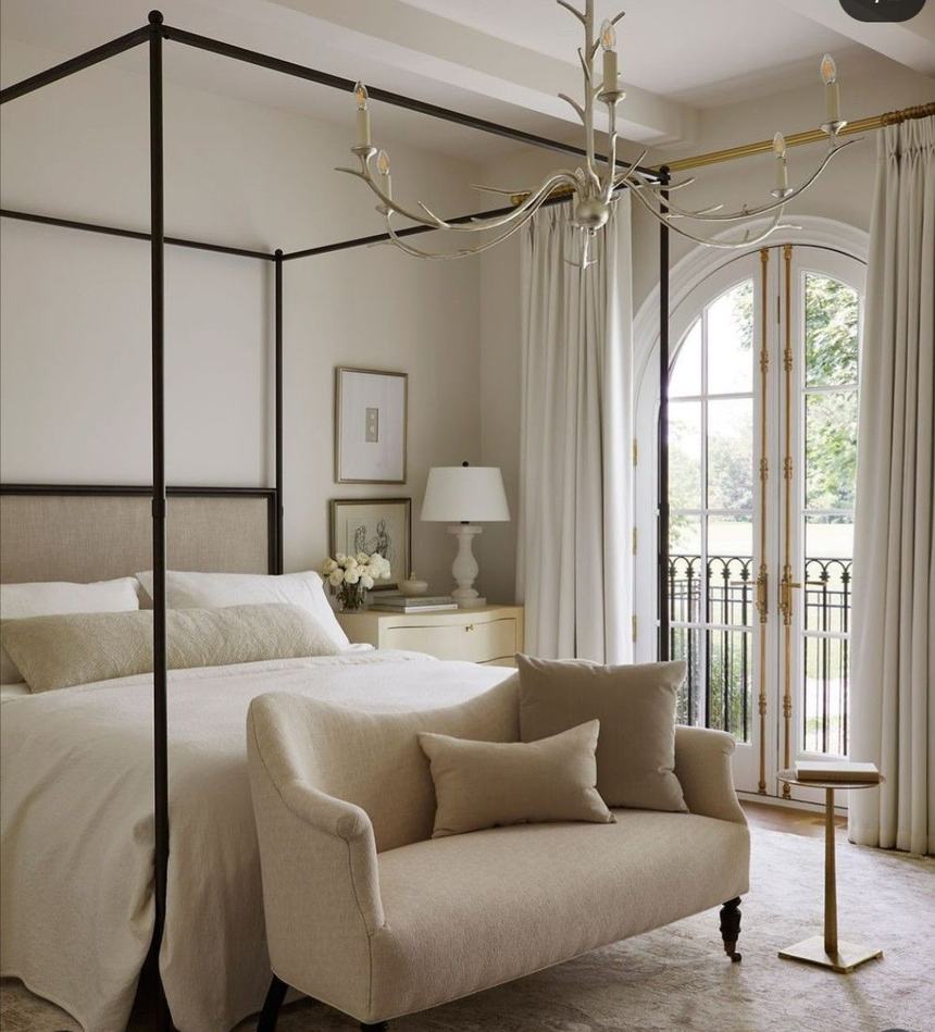 Iron canopy bed with layered white bedding and a linen settee in a bright primary suite