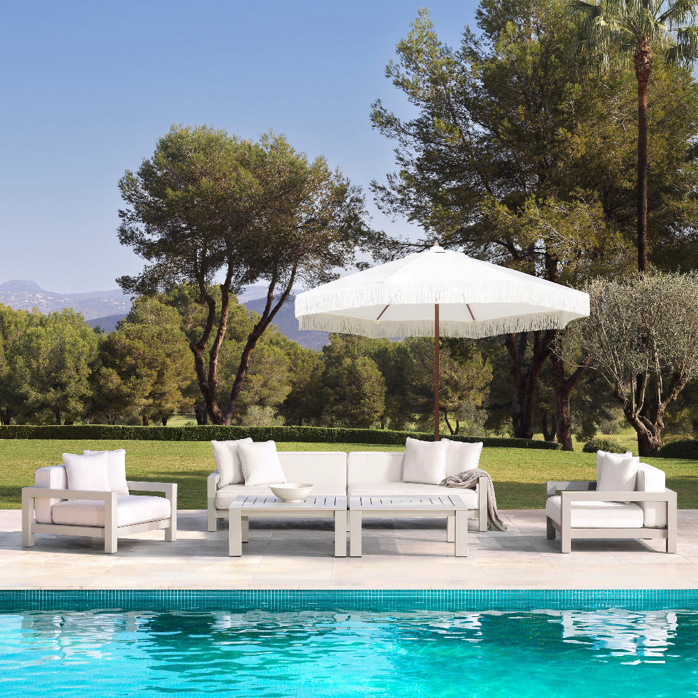 Outdoor patio set with chairs and a table by a pool, surrounded by trees and mountains.
