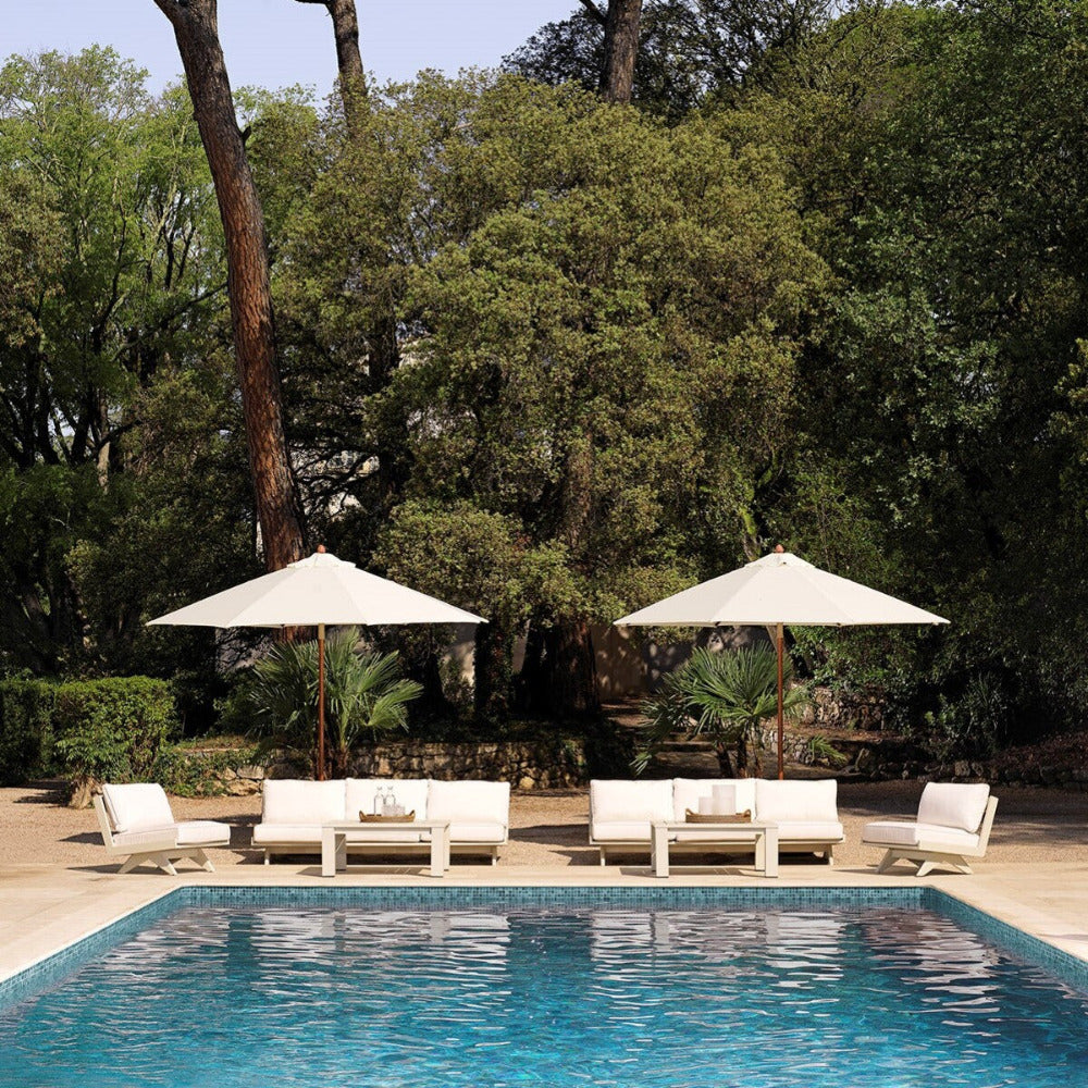Outdoor pool with white chairs and umbrellas, surrounded by trees.