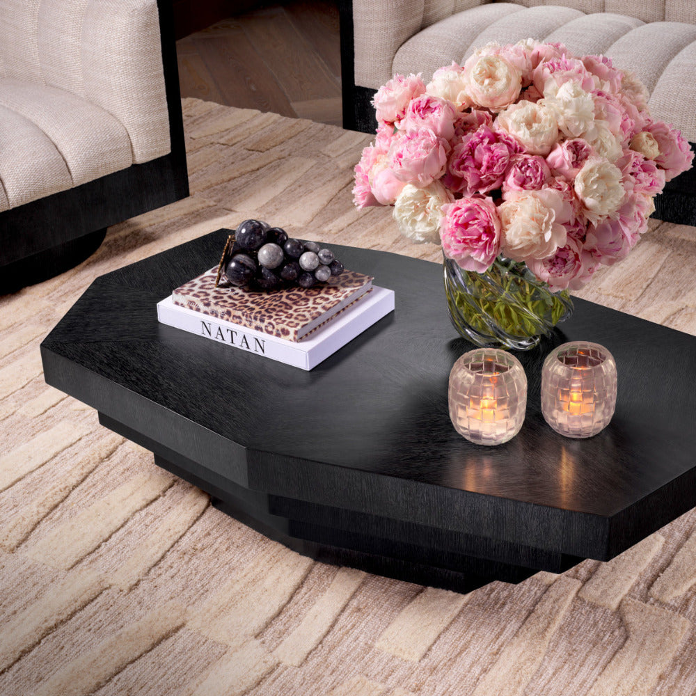 Black coffee table with decorative items including a vase of pink and white flowers, candles, and books.