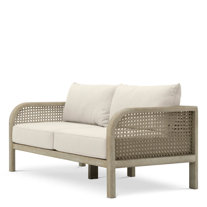 Beige wicker outdoor sofa with white cushions on a white background