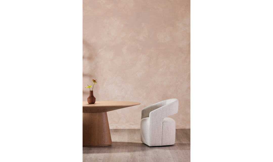 Modern white chair and round wooden table against a beige wall.