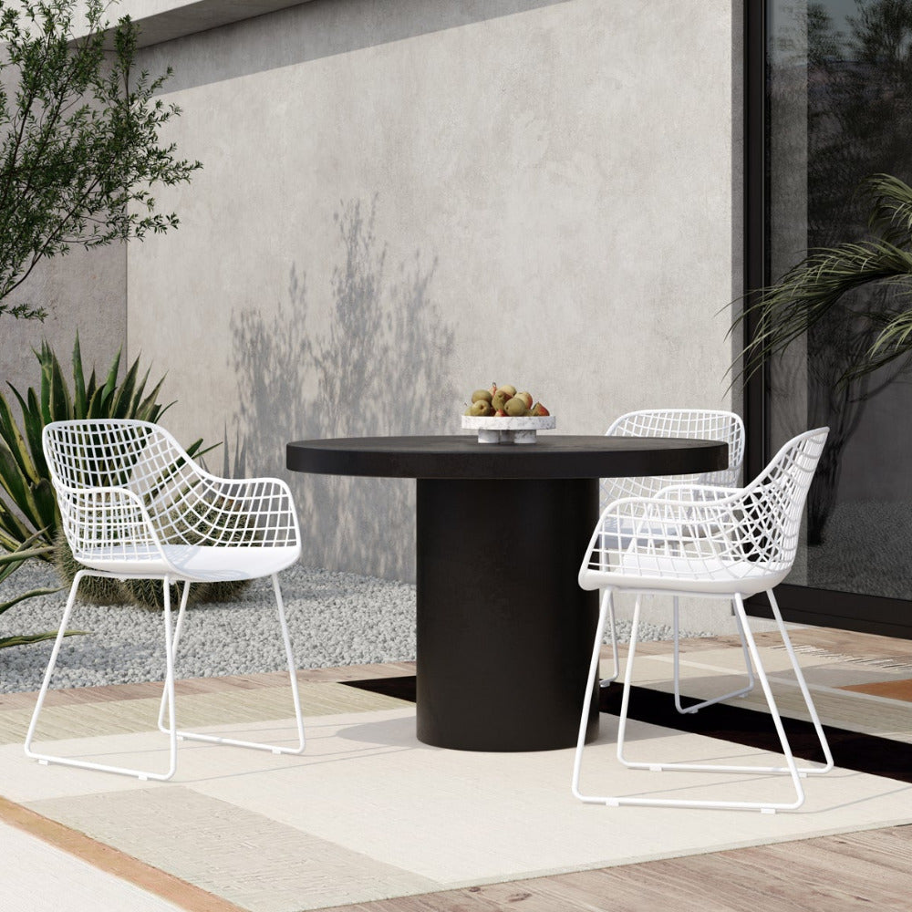 Outdoor patio set with a black round table and white wire chairs, surrounded by plants.
