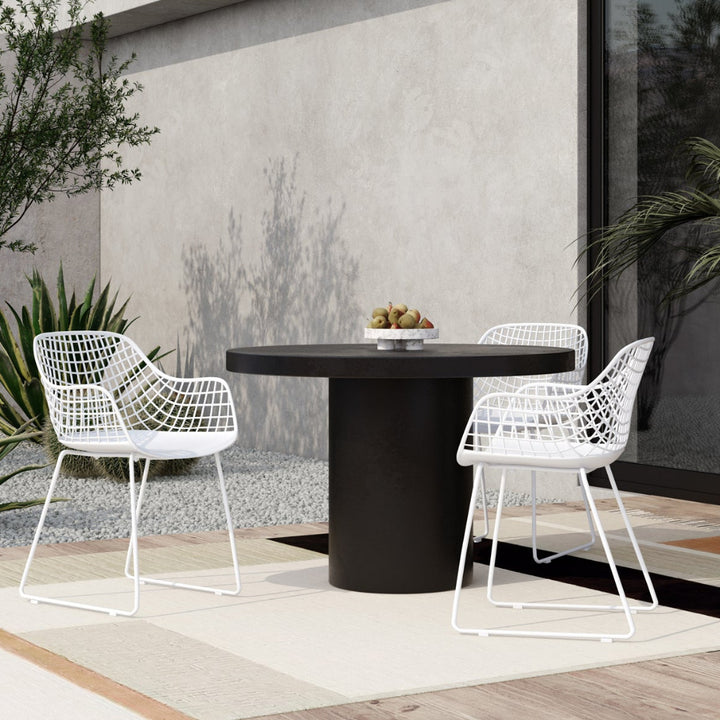 Outdoor patio set with a black round table and white wire chairs, surrounded by plants.