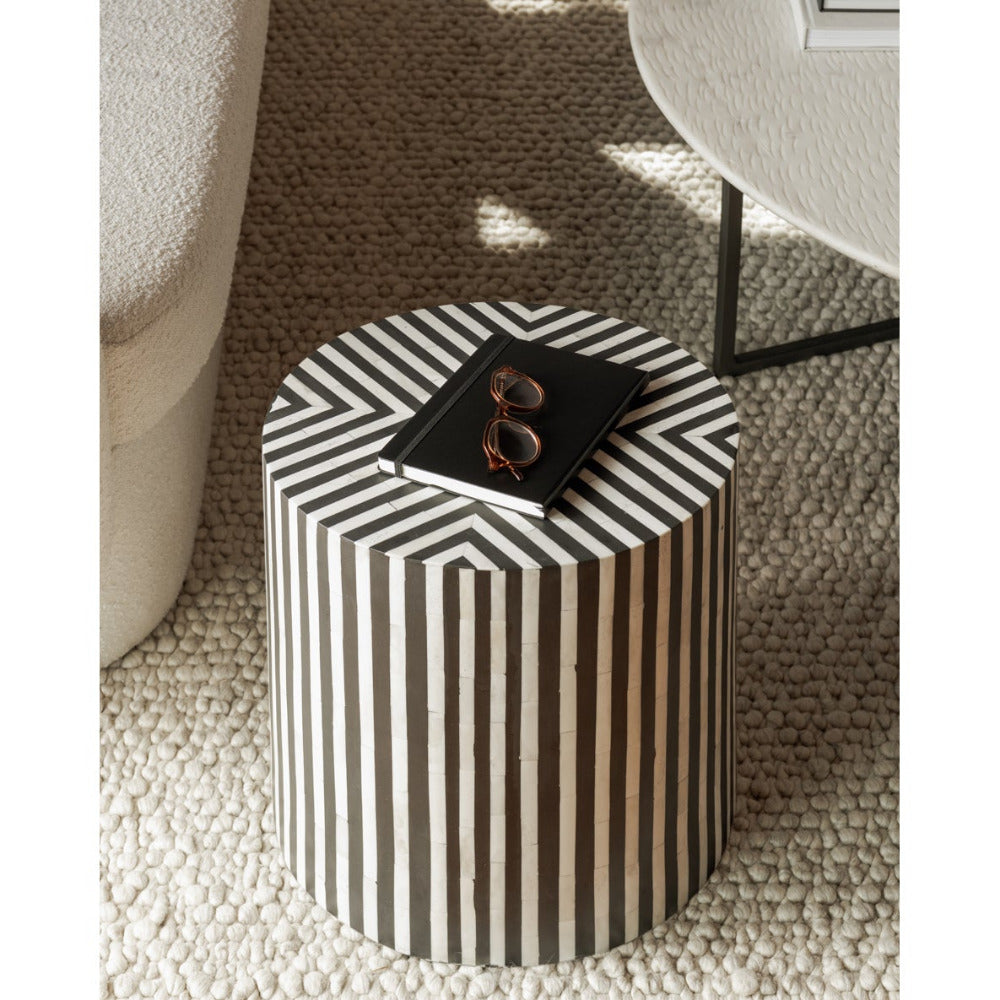 Black and white striped cylindrical side table on a textured surface
