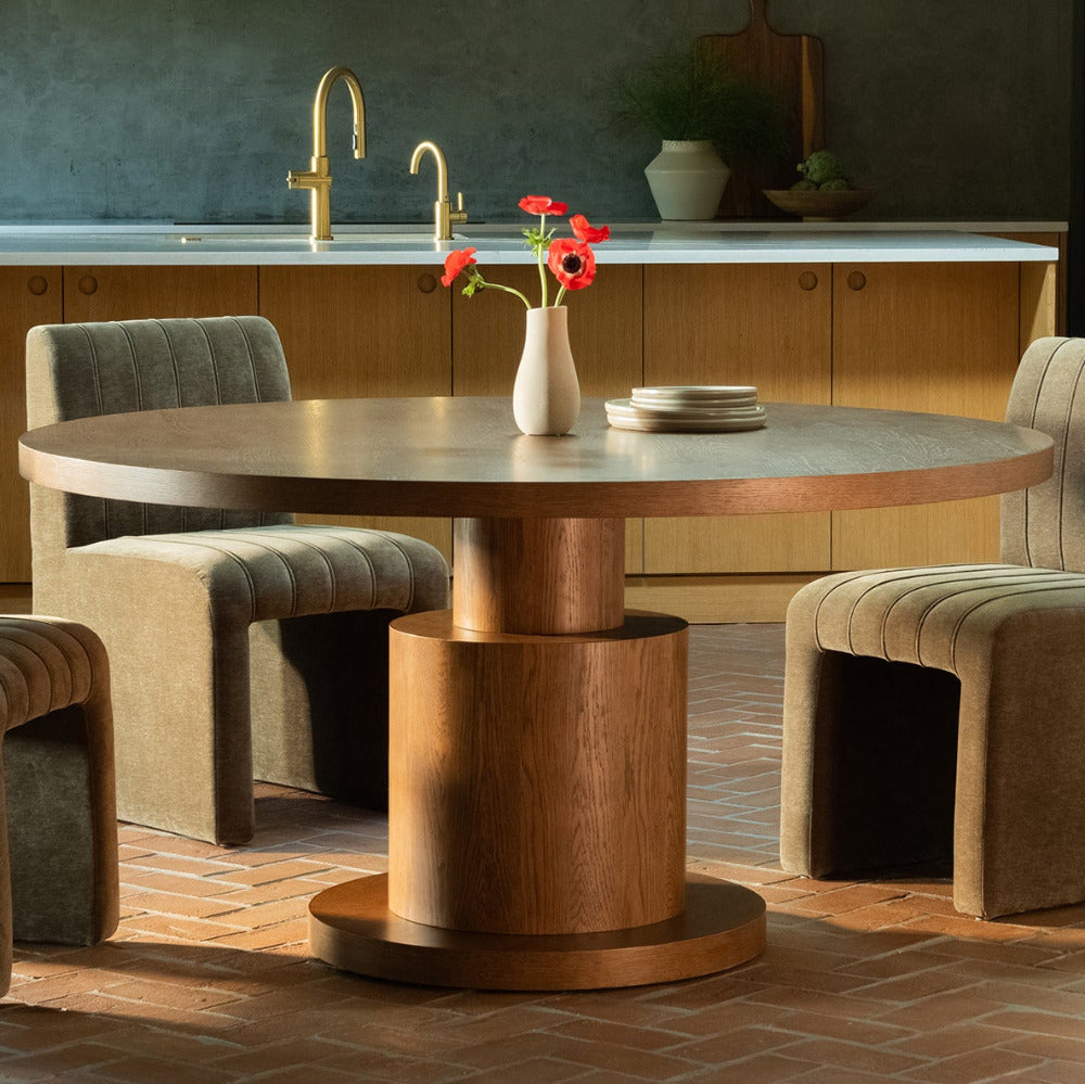 Modern dining area with a round wooden table and upholstered chairs in a kitchen setting.