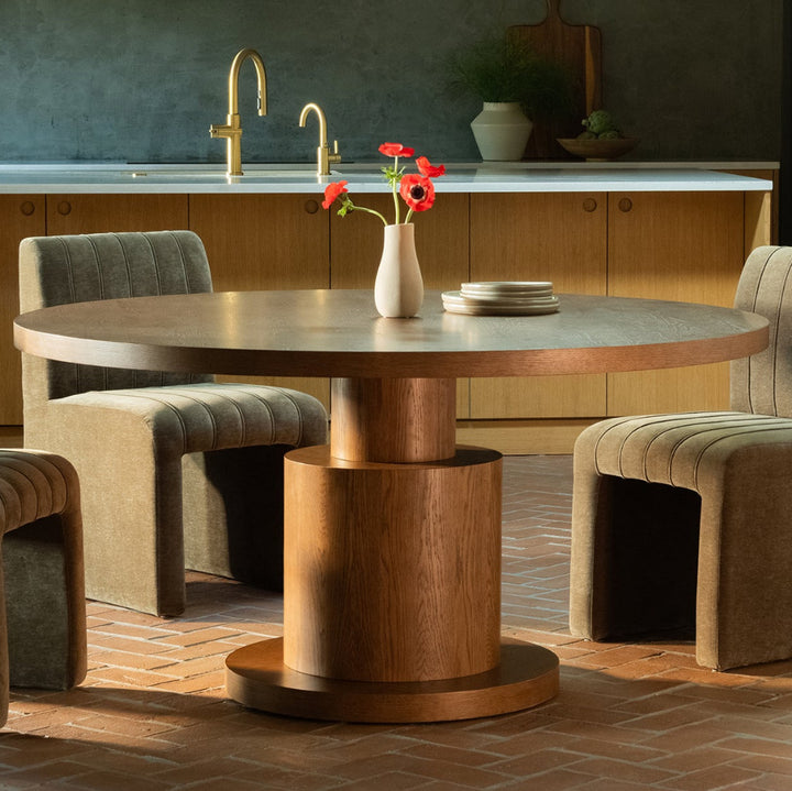 Modern dining area with a round wooden table and upholstered chairs in a kitchen setting.