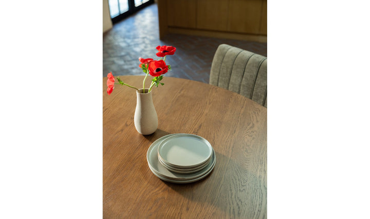 Stack of plates on a wooden table with a vase of red flowers.