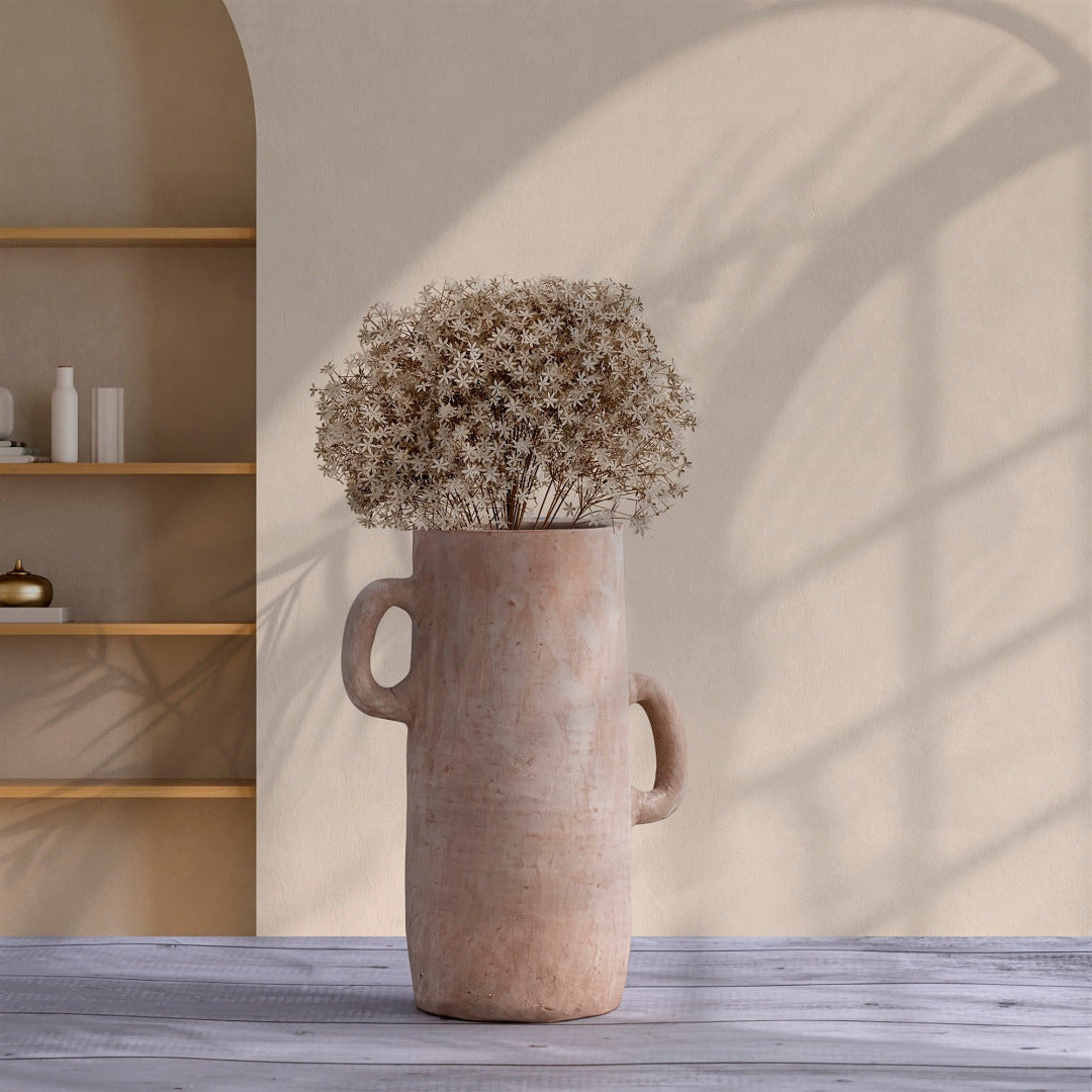 Terracotta vase with flowers on a wooden surface against a neutral wall.