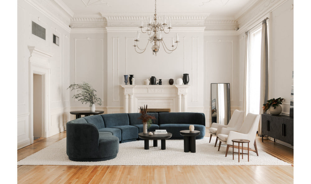 Modern living room with a blue sectional sofa, white chairs, and a chandelier.