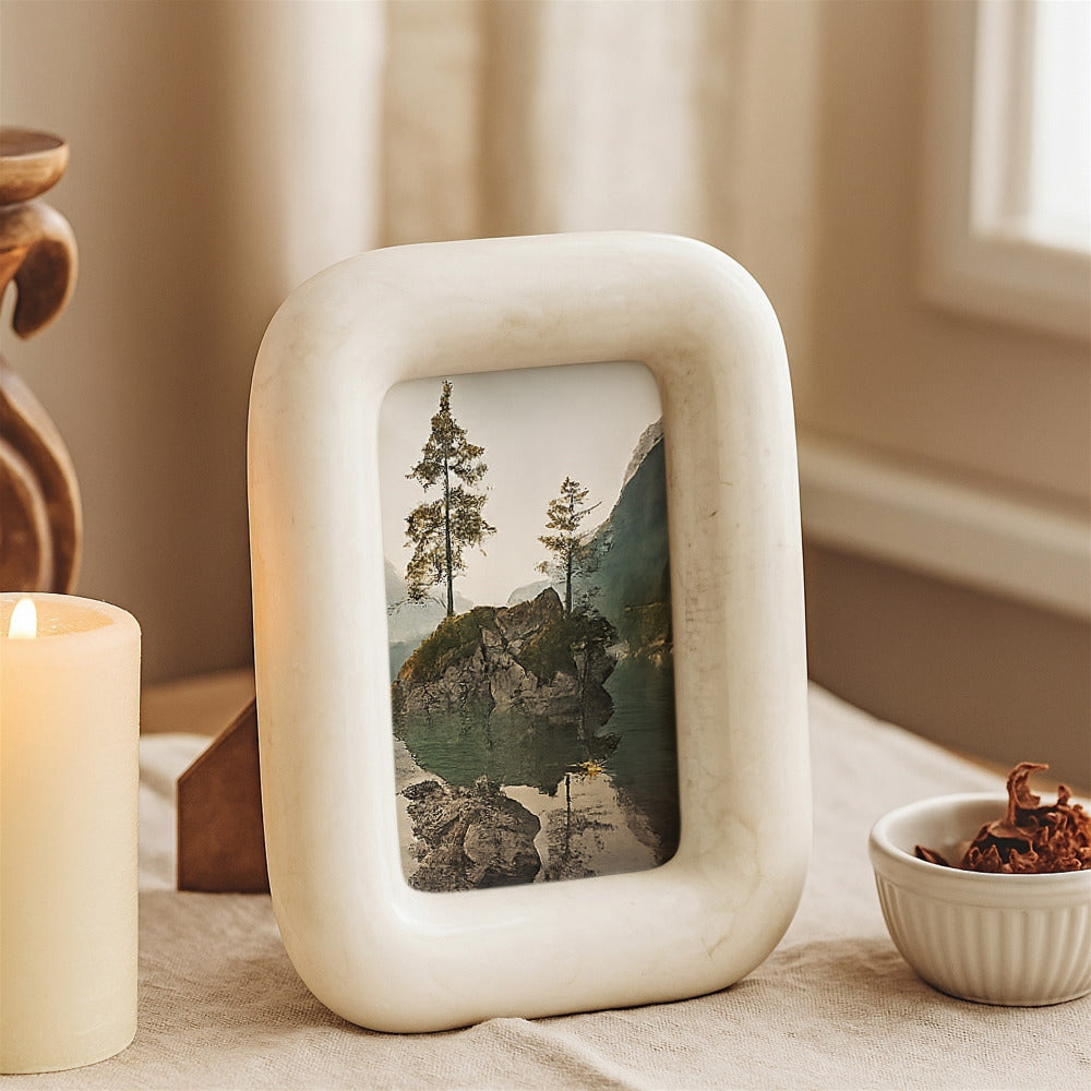 White ceramic photo frame with a scenic picture on a table with a candle and small bowl.