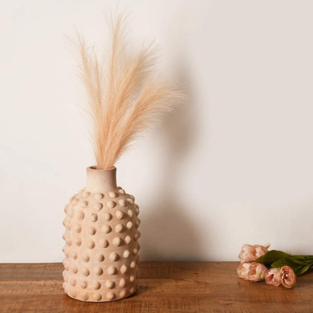 Textured beige vase with dried plants on a wooden surface