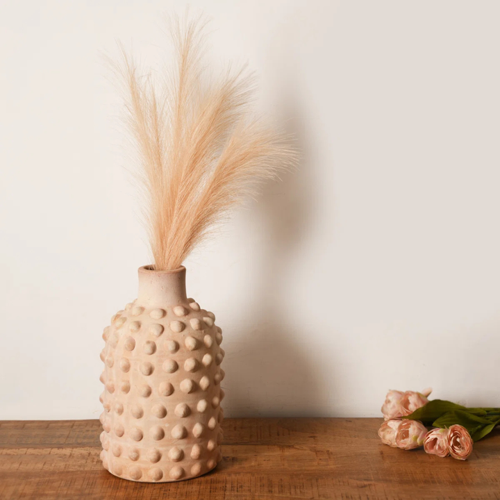 Textured beige vase with dried plants on a wooden surface