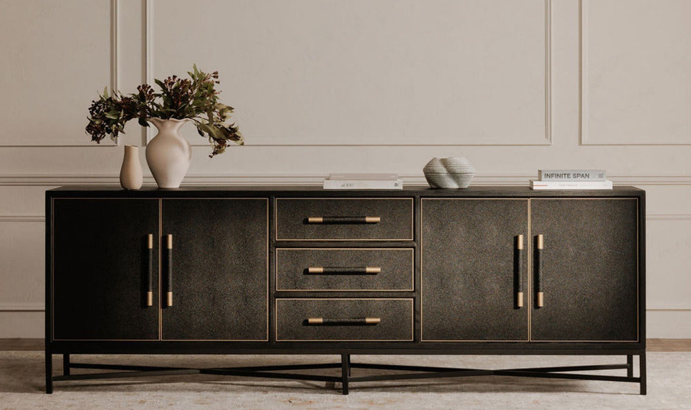 Black sideboard with gold handles against a neutral wall.
