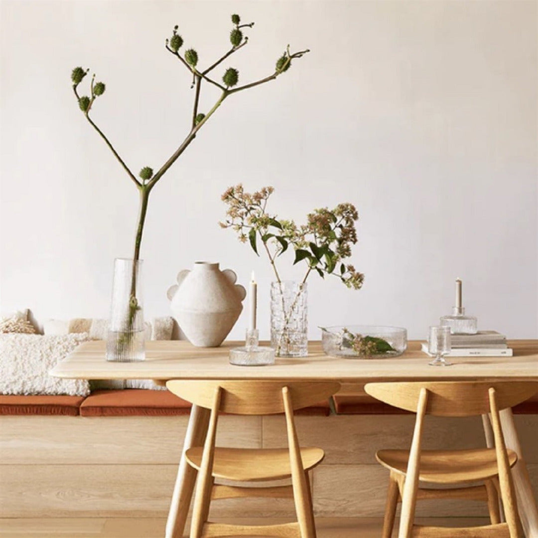 Dining area with wooden table, chairs, and decorative vases on a light background