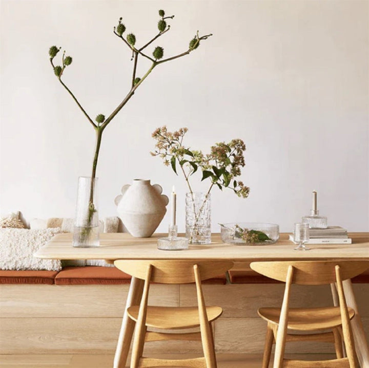Dining area with wooden table, chairs, and decorative vases on a light background