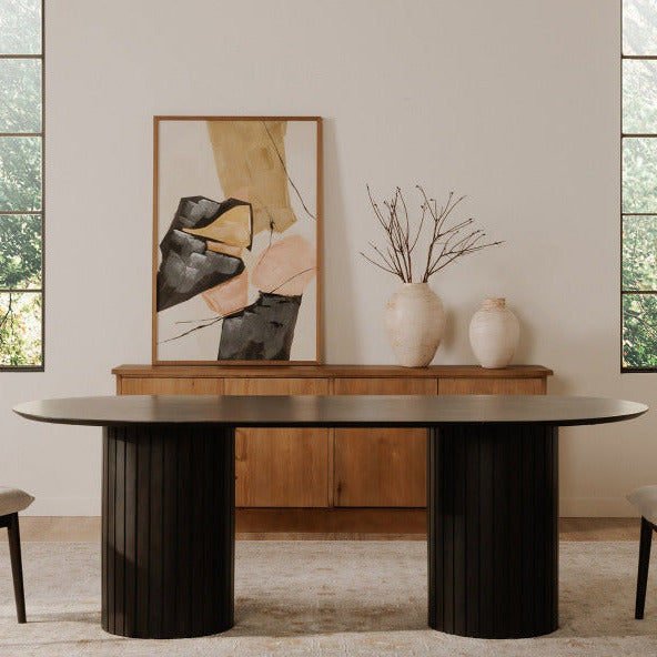 Dining room with a black oval table, beige chairs, and abstract art on a wooden console.