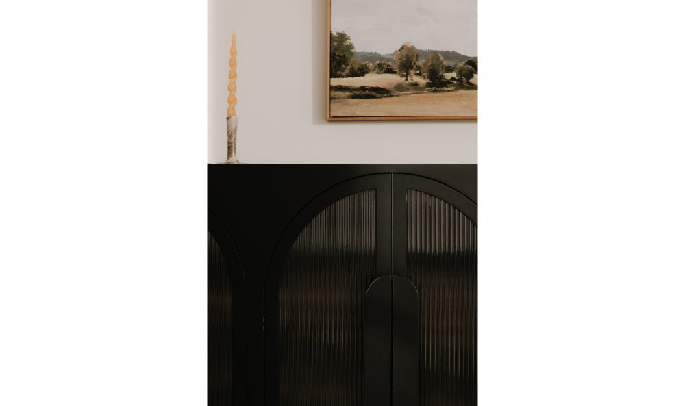 Black sideboard with a framed landscape picture above it on a white wall.
