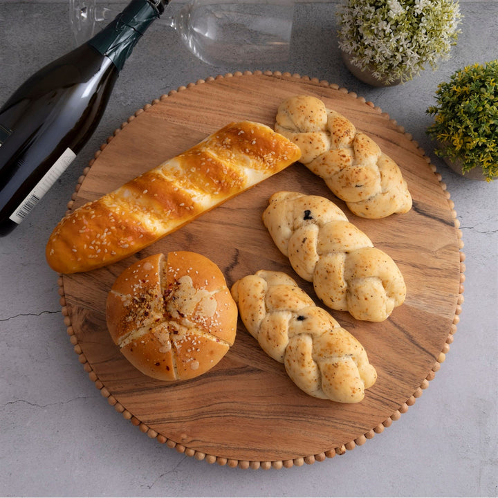 Assorted bread loaves on a wooden beaded plate with a bottle of wine in the background.