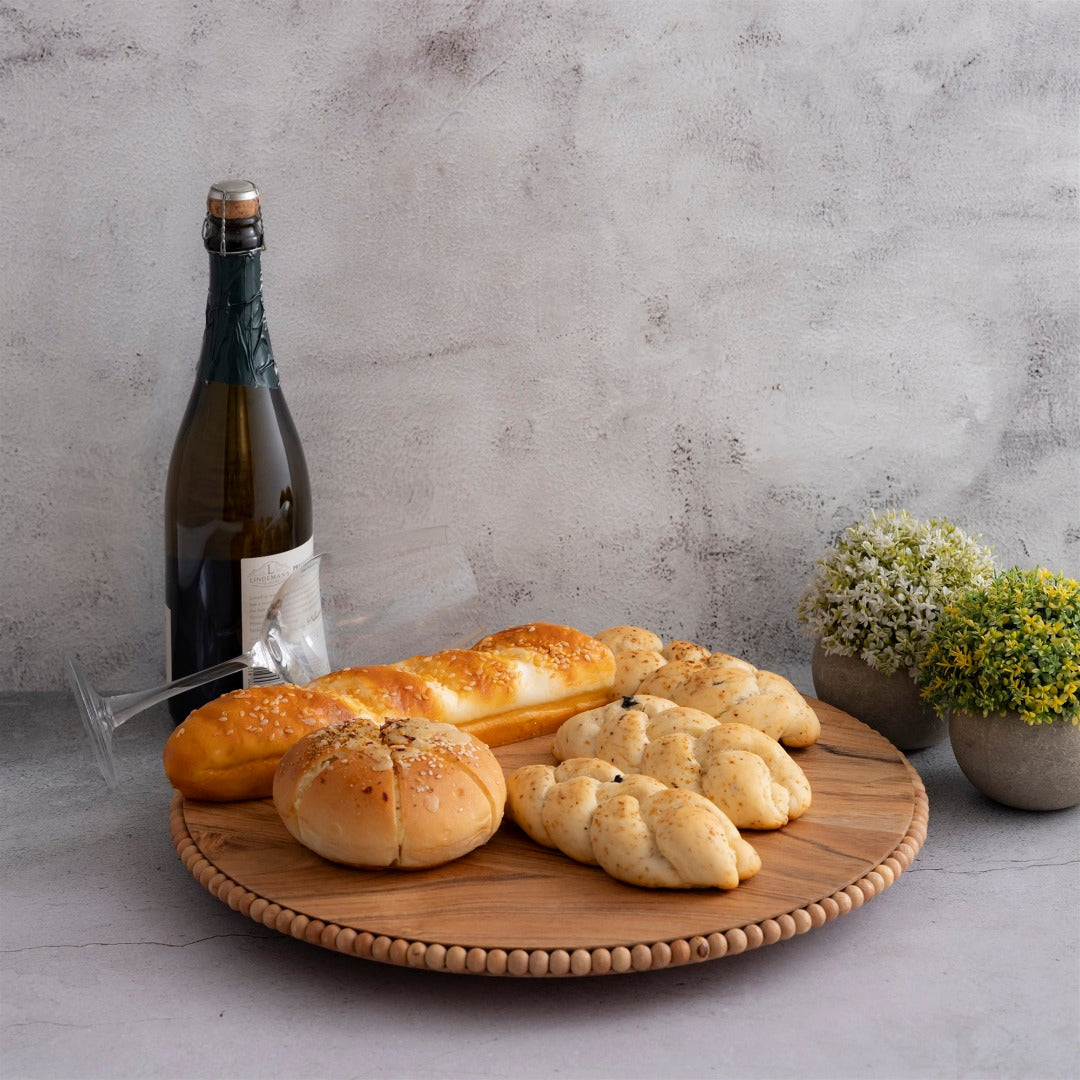 Wooden beaded plate with bread and a bottle of wine on a gray surface with a concrete wall background.