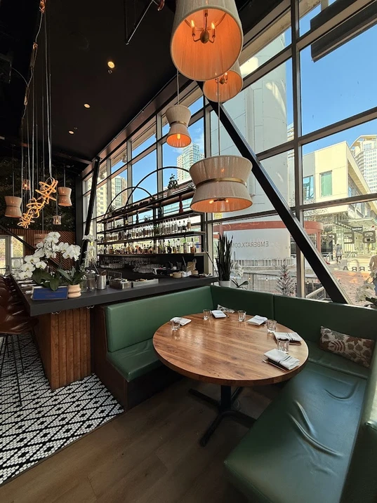 Restaurant bar with green banquettes, orchids and arched windows over downtown Houston
