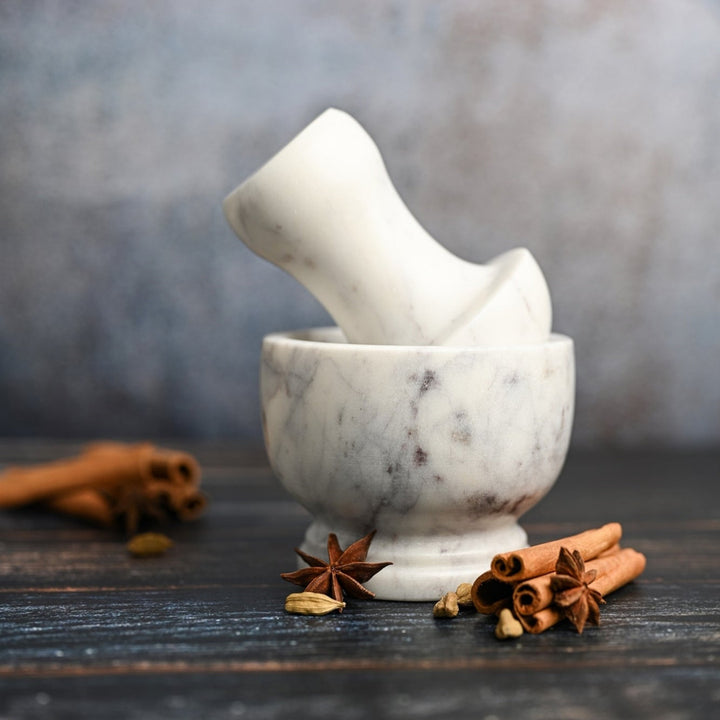 White marble mortar and pestle on a wooden surface with cinnamon sticks.