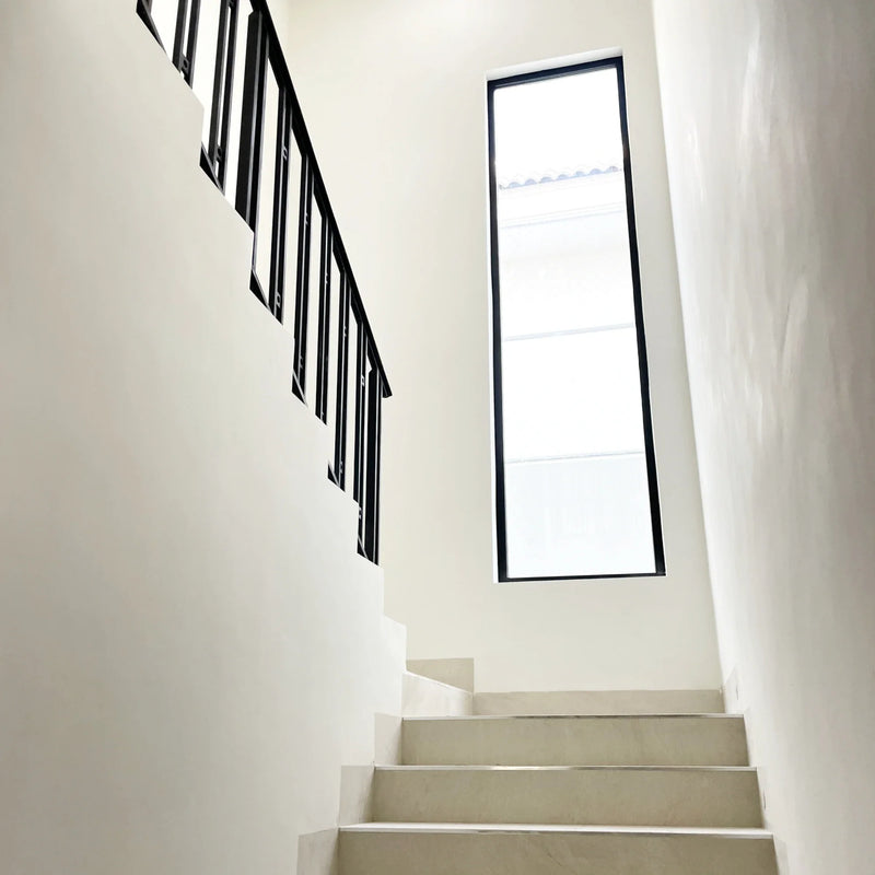 Sculptural white staircase with a slim black metal railing and full-height window