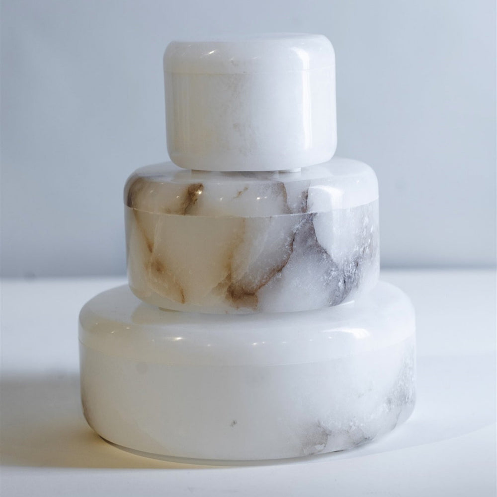 Alabaster cylindrical boxes on a white surface with a light gray background