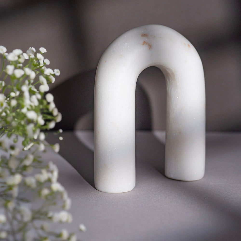 White arch-shaped marble figurine on a gray surface with a blurred background