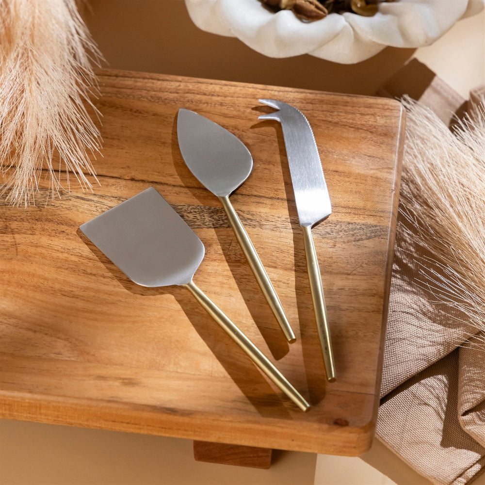 Three metal cheese tools on a wooden board with a neutral background