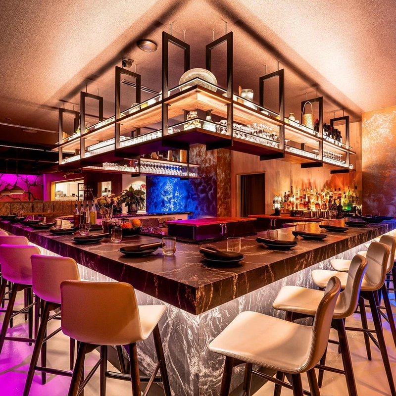 Sushi bar with a backlit bottle display, marble counter and jewel-toned lighting
