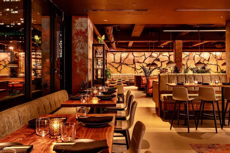 Restaurant dining room with a stacked stone feature wall, walnut millwork and olive banquettes