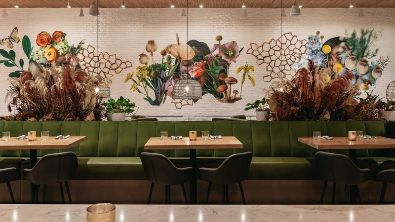 Restaurant banquette seating beneath a botanical mural on whitewashed brick