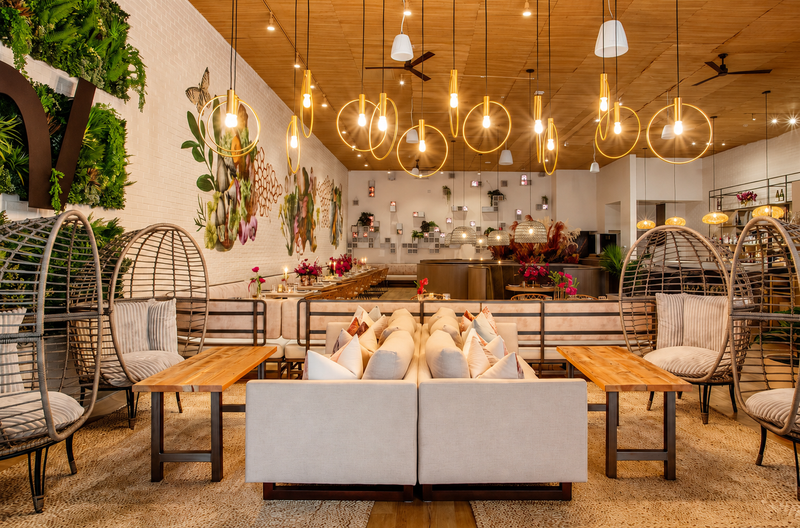 Restaurant with rattan cocoon chairs, brass globe pendants and layered greenery