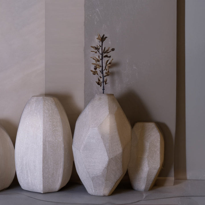 Set of three textured glass vases with plants against a neutral wall.